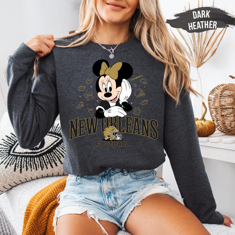 A woman wearing a grey sweatshirt with a Minnie Mouse graphic and text that says "New Orleans Football" is sitting in a room with a pumpkin decoration.