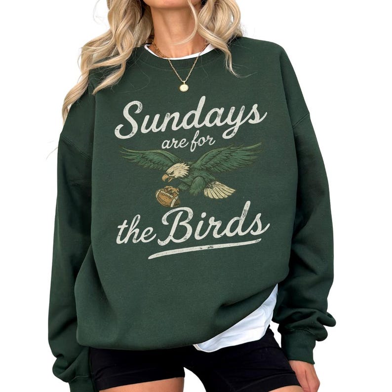 A woman wearing a green sweatshirt with the text "Sunday's are for the Birds" printed on it.