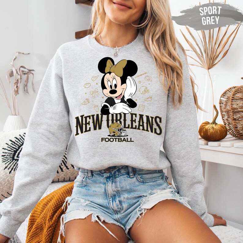 A woman wearing a grey sweatshirt with a cartoon character and text related to New Orleans football.