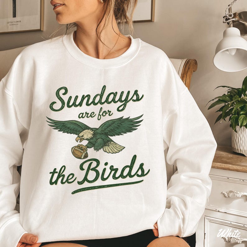 A woman wearing a white sweatshirt with a graphic design that says "Sunday are for the Birds" and features an eagle holding a football.