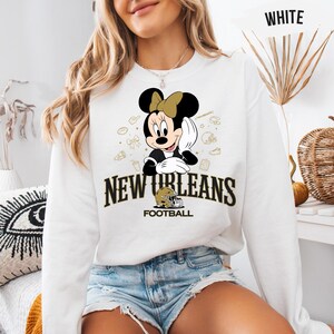 A woman wearing a white sweatshirt with a Minnie Mouse graphic and text that says "New Orleans Football".