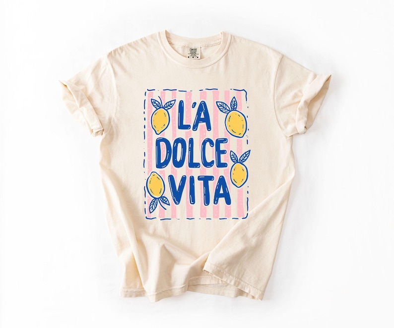 A white t-shirt with a graphic design featuring the text "LA Dolce Vita" surrounded by lemon and lime illustrations.