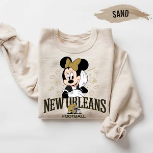 A beige sweatshirt with a cartoon image of Minnie Mouse and the text "New Orleans Football" printed on it.