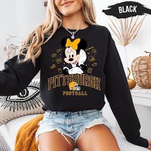 May include: Black sweatshirt featuring Minnie Mouse in a football-themed design. The graphic includes a yellow bow, football helmet, and the text "PITTSBURGH FOOTBALL" in yellow. The sweatshirt is a crew neck style.