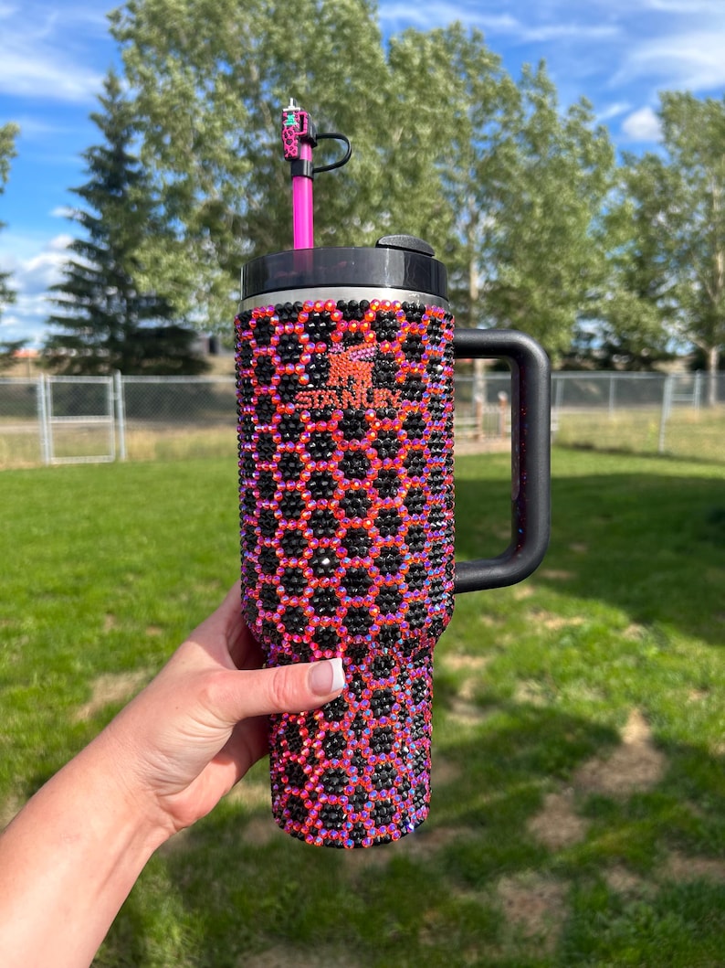 Może przedstawiać: Czarny i r&oacute;żowy kubek ze stali nierdzewnej z wzorem plastra miodu pokrytym kryształkami. Kubek ma czarny uchwyt i pokrywkę z otworem na słomkę.