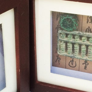 May include: Two framed antique Chinese abacuses, one with a green jade bead and the other with a green jade charm. Both are displayed on a brown background with Chinese characters.