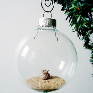 May include: A clear glass Christmas ornament with a small burlap sack filled with gold glitter inside.