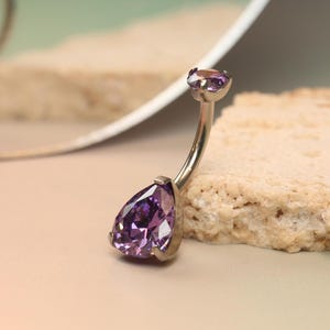 May include: A silver belly button ring with two purple pear-shaped gems.