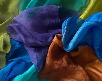 May include: A collection of sheer fabric scarves in various colors, including teal, green, blue, purple, and brown. The scarves are arranged in a loose pile, with some of the fabric overlapping.