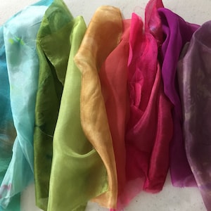 May include: A set of eight silk scarves in various colors, including orange, teal, green, gold, red, pink, purple, and lavender. The scarves are folded and arranged in a row.