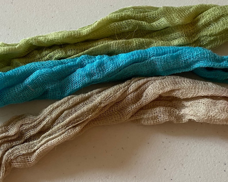 K&ouml;nnte beinhalten: Drei Stoffst&uuml;cke in verschiedenen Farben: hellgr&uuml;n, t&uuml;rkisblau und beige. Der Stoff ist ein d&uuml;nnes, durchsichtiges Material mit einer gewebten Textur.