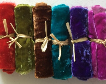 May include: Seven rolls of colorful velvet fabric in shades of red, green, brown, teal, purple, and pink. Each roll is tied with natural raffia. The fabric has a soft, plush texture, ideal for crafting and sewing projects.