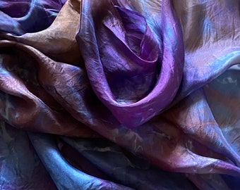 May include: A sheer fabric scarf in shades of purple, blue, and brown. The fabric is gathered and draped, creating a soft and flowing look.