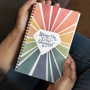 Puede incluir: Un cuaderno espiral con un diseño de arcoíris colorido y el texto "Shine On You Crazy Diamond" en forma de diamante.