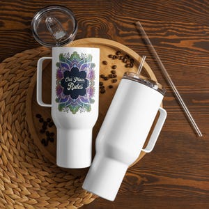 Puede incluir: Dos tazas de viaje de acero inoxidable blanco con tapas y asas. Una taza tiene un diseño de mandala colorido con el texto "Our Place, Our Rules".