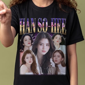 Könnte beinhalten: Schwarzes T-Shirt mit dem Text "HAN SO-HEE" in einem Farbverlauf. Das Shirt zeigt mehrere Bilder einer Frau. Die Person im Bild zeigt nach links.