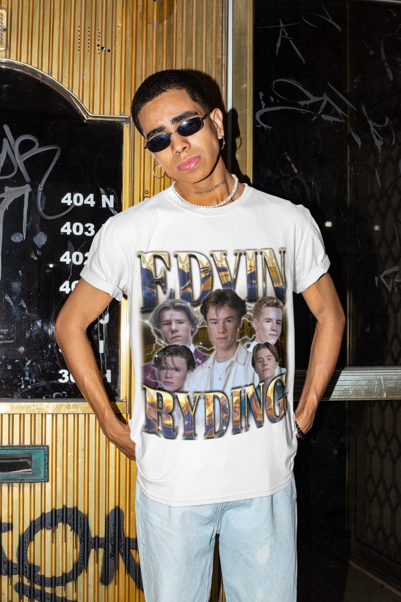Op de afbeelding: Wit T-shirt met een goud-blauwe afbeelding van de tekst "EDVIN RYDING" en een collage van zes jonge mannen. Het T-shirt wordt gedragen door een persoon met een zonnebril en een lichtblauwe jeans.