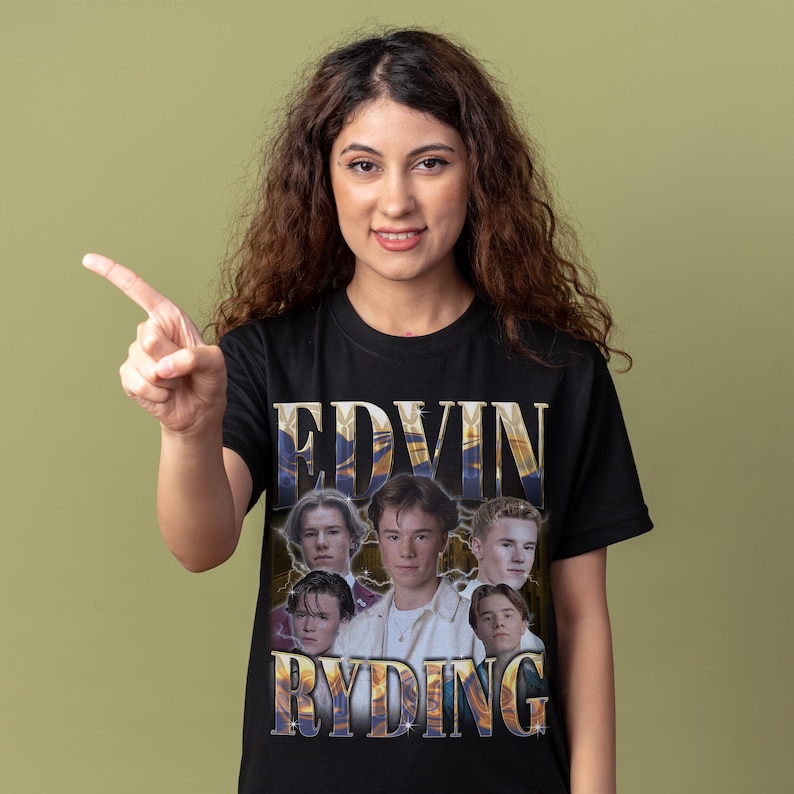 Op de afbeelding: Zwart t-shirt met een goud en blauw ontwerp met de tekst "EDVIN RYDING" en een groep jonge mannen. Het ontwerp heeft een vintage, licht vervaagde uitstraling.