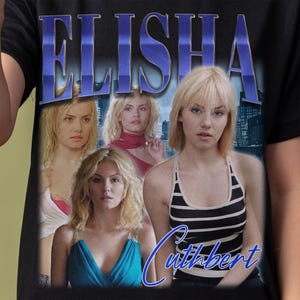 May include: A black t-shirt with a blue and white graphic print of Elisha Cuthbert's face and the text "Elisha Cuthbert".
