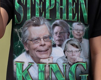 May include: Black t-shirt featuring a graphic of Stephen King in multiple images, with the name "STEPHEN KING" in large, green, stylized letters. The design includes lightning bolts and a vintage aesthetic.