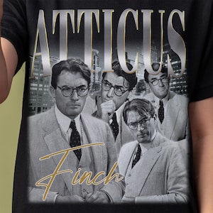 May include: A black t-shirt with a graphic print of Atticus Finch from the novel To Kill a Mockingbird. The graphic features a collage of images of Atticus Finch in different poses, with the text "Atticus Finch" in gold lettering at the top.