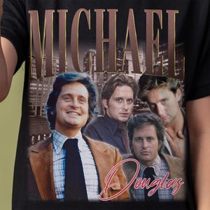 May include: Black t-shirt featuring a vintage-style graphic of Michael Douglas with the name "MICHAEL" above and "Douglas" in cursive script below. The graphic includes multiple images of the actor.