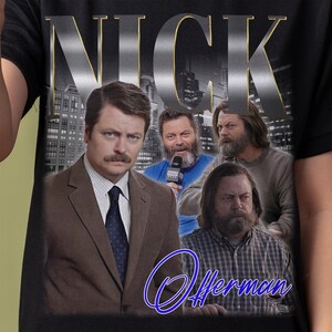 May include: Black t-shirt featuring a graphic of Nick Offerman's face and the word "NICK" in large, silver letters. The graphic also includes a cityscape background and the text "Offerman" in blue cursive.