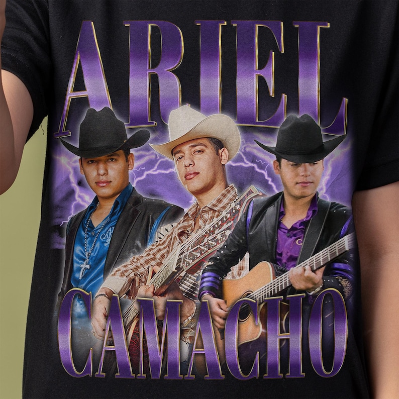 May include: Black t-shirt featuring a graphic of three men in cowboy hats, each holding a guitar. The text "ARIEL" and "CAMACHO" are in purple, with a lightning bolt design in the background.