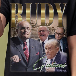 Könnte beinhalten: Ein schwarzes T-Shirt mit einem Vintage-Grafikdruck mit dem Namen "Rudy Giuliani" in goldenen Buchstaben. Die Grafik enthält auch Bilder von drei Männern, von denen einer einen Anzug und eine Krawatte trägt und ein Namensschild mit der Aufschrift "Rudy Giuliani" trägt.