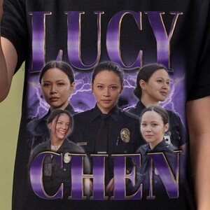May include: Black t-shirt featuring a graphic of a woman in a police uniform, with the name "LUCY CHEN" in purple text. The design includes multiple images of the woman against a purple lightning background.
