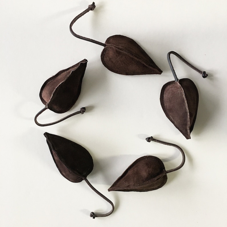 Puede incluir: Cuatro bolsas de gamuza marr&oacute;n en forma de hoja con lazos de cuero. Las bolsas est&aacute;n colgando de los lazos.