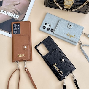 May include: A collection of leather phone cases in brown, black, and light blue. Each case features a cardholder and a strap. The brown case is embossed with "A&R", the black case with "Jacob" and a heart, and the blue case with "loyal".