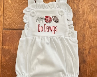 May include: White baby romper with ruffle trim and straps. The front features embroidered images of a bulldog, a red pompom, and a football, with the text "Go Dawgs" in red.