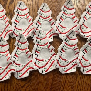 May include: Nine white felt Christmas tree ornaments with red and green embroidery. The ornaments have a circular opening in the center.