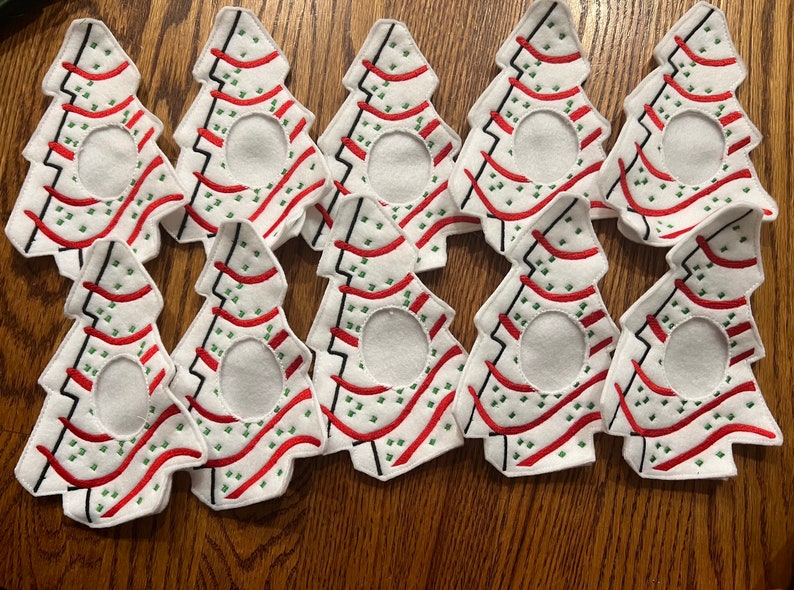 May include: Nine white felt Christmas tree ornaments with red and green embroidery. The ornaments have a circular opening in the center.