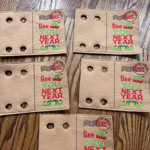 May include: Five brown felt ornaments with a red and green elf design and the text "See You Next Year". Each ornament has a white stamp with the text "North Pole Dec".
