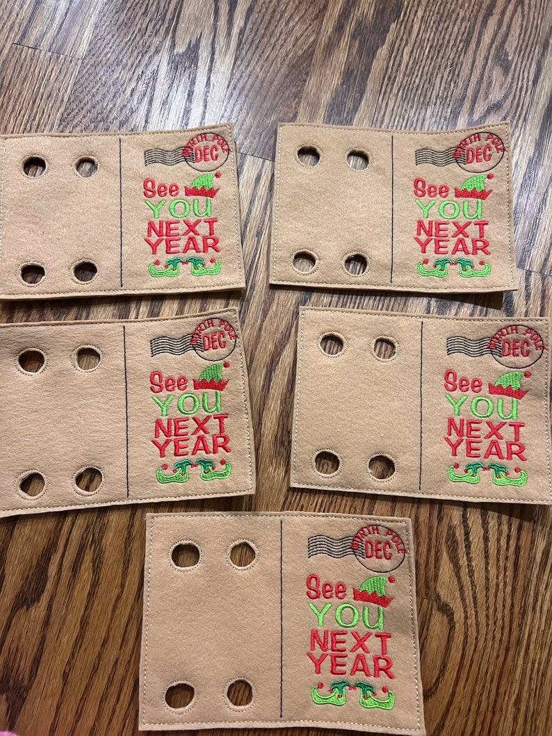 May include: Five brown felt ornaments with a red and green elf design and the text "See You Next Year". Each ornament has a white stamp with the text "North Pole Dec".