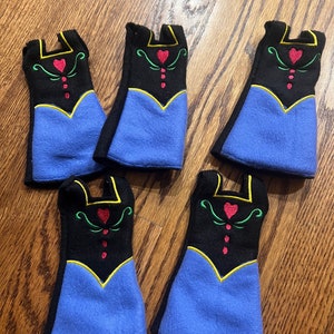 May include: Five felt doll dresses in blue, black, and yellow with red and green embroidery. The dresses feature a heart design and are perfect for a dollhouse or playset.