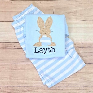 Może przedstawiać: Piżama w paski jasnoniebieskie i białe z jasnoniebieską koszulą z brązowym błyszczącym kr&oacute;likiem z niebiesko-białym paskowanym ogonem i imieniem "Layth" wyszytym z przodu.