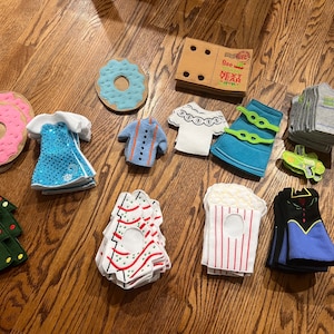 May include: A collection of felt play food and clothing items, including a donut, a Christmas tree, a popcorn box, a dress, a shirt, and a skirt. The items are all handmade and have a variety of colors and patterns.