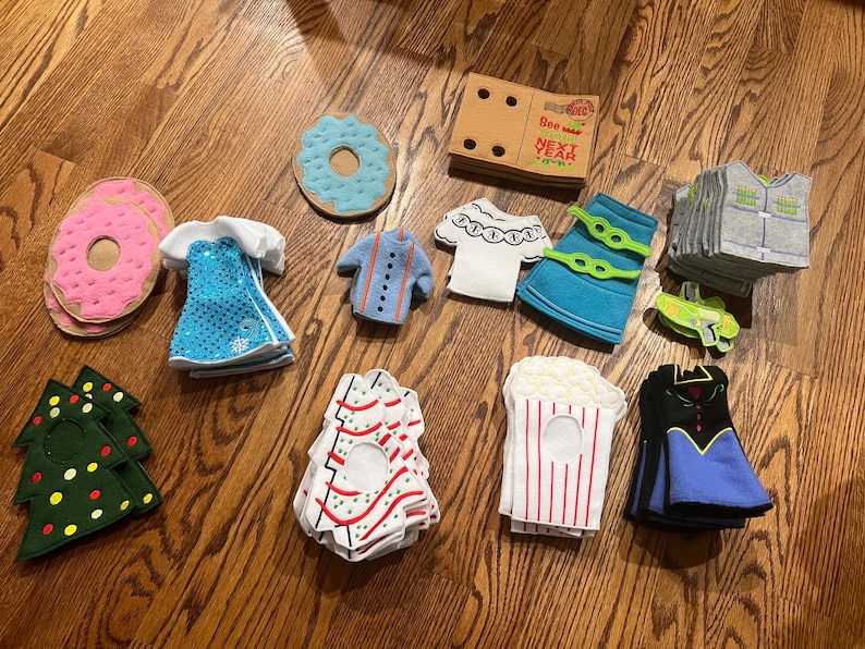 May include: A collection of felt play food and clothing items, including a donut, a Christmas tree, a popcorn box, a dress, a shirt, and a skirt. The items are all handmade and have a variety of colors and patterns.