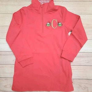 May include: Red long-sleeve pullover with a red and white checkered collar. The pullover has a zipper and features two embroidered green Grinch faces wearing Santa hats and a gold letter C.
