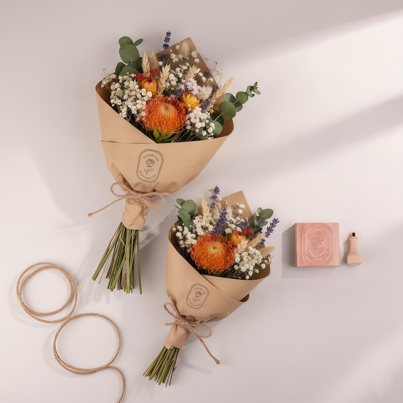 Pu&ograve; includere: Due bouquet di fiori secchi avvolti in carta marrone, legati con spago. I bouquet presentano protea arancioni, gipsofila bianca ed eucalipto verde. Sono presenti anche una saponetta e un flaconcino.