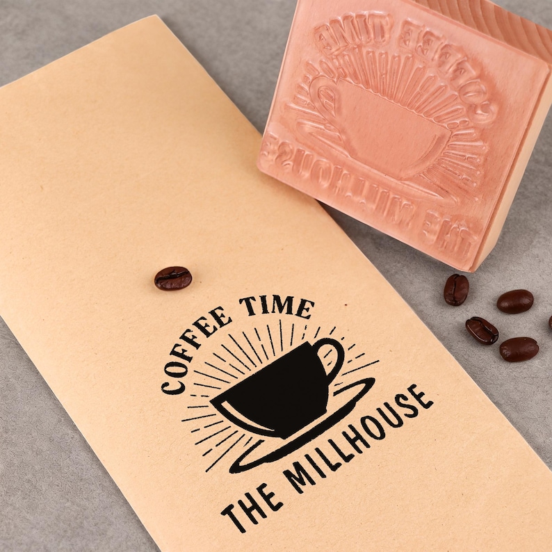 Pu&ograve; includere: Un sacchetto di carta beige con la scritta "COFFEE TIME THE MILLHOUSE" e una grafica di tazza di caff&egrave; nera. &Egrave; presente anche un timbro di legno con un disegno di tazza di caff&egrave; e chicchi di caff&egrave;.