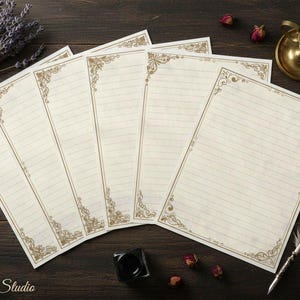 May include: Cream-colored stationery with gold decorative borders and lined pages. A bundle of lavender, a brass candle holder with a lit candle, and a quill pen are arranged on a dark wooden surface. The text "Dishley Studio" is visible.