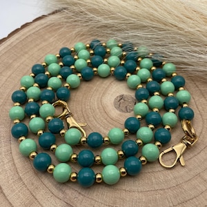 Puede incluir: Collar de cuentas con cuentas de color verde azulado y verde menta alternadas, intercaladas con pequeñas cuentas doradas. El collar tiene cierres dorados en cada extremo. Las cuentas están dispuestas en tres hilos.
