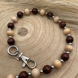 Könnte beinhalten: Eine Hundeleine mit abwechselnd dunkelbraunen und hellbraunen Holzperlen, verbunden durch kleine silberfarbene Metallperlen. Die Leine hat einen silberfarbenen Metallverschluss zum einfachen Befestigen am Halsband des Hundes.