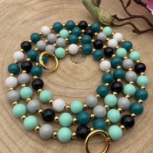 Könnte beinhalten: Eine mehrreihige Halskette aus Holzperlen in den Farben Teal, Mintgrün, Grau und Schwarz. Die Halskette hat goldfarbene Metallverschlüsse.