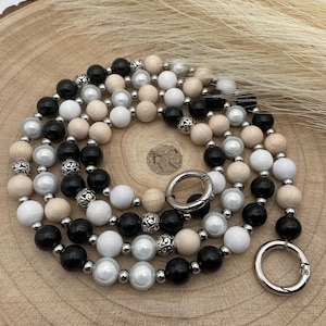 Könnte beinhalten: Eine schwarze, weiße und beige Perlen-Telefonkette mit silbernen Metallverschlüssen. Die Kette besteht aus Holzperlen, Perlenperlen und schwarzen Perlen.