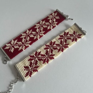 Puede incluir: Dos pulseras de cuentas con fondo blanco y motivos florales rojos. Las pulseras tienen cierres plateados.